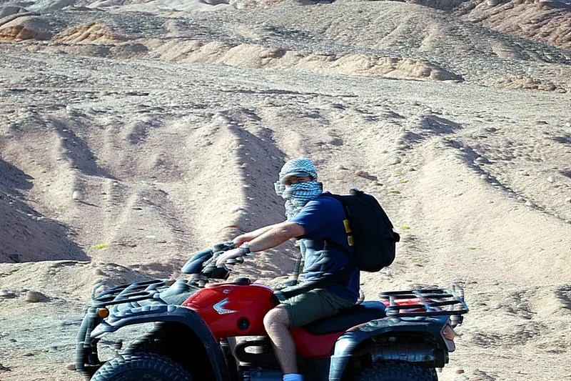 A quad rider crossing rocky desert hills